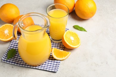 Photo of Tasty orange juice in jug, glass and citrus fruits on light textured table. Space for text