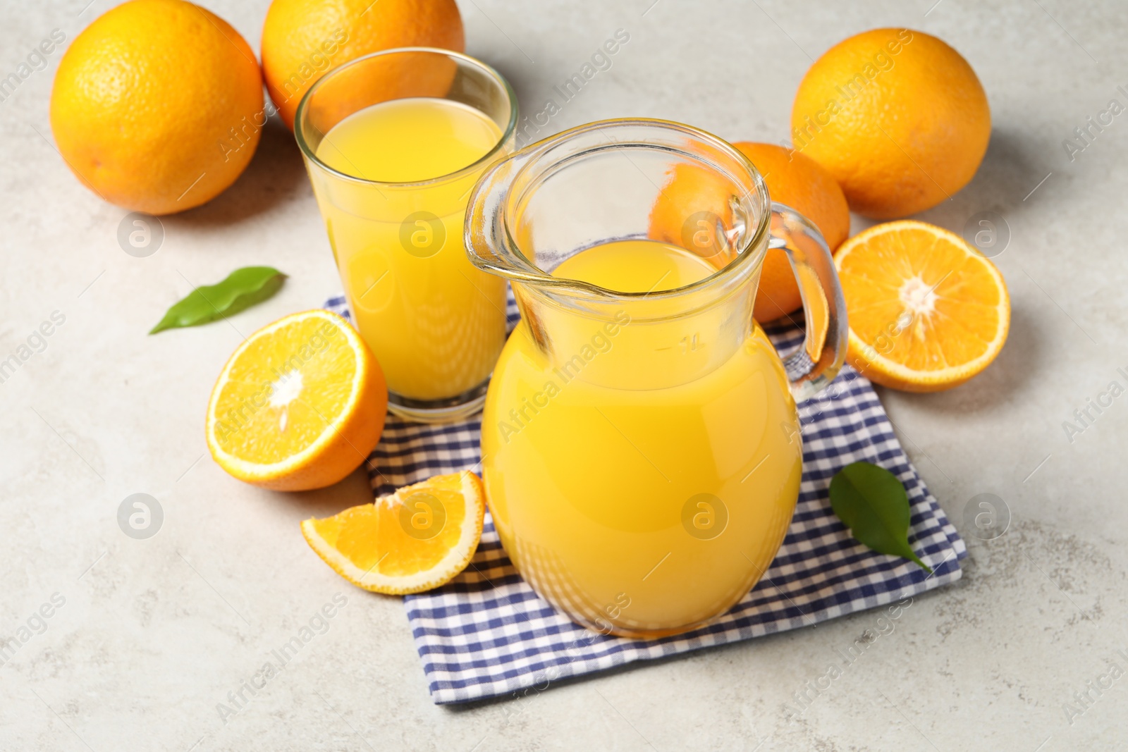 Photo of Tasty orange juice in jug, glass and citrus fruits on light textured table