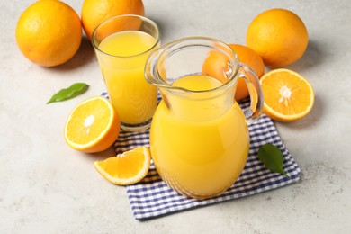 Photo of Tasty orange juice in jug, glass and citrus fruits on light textured table