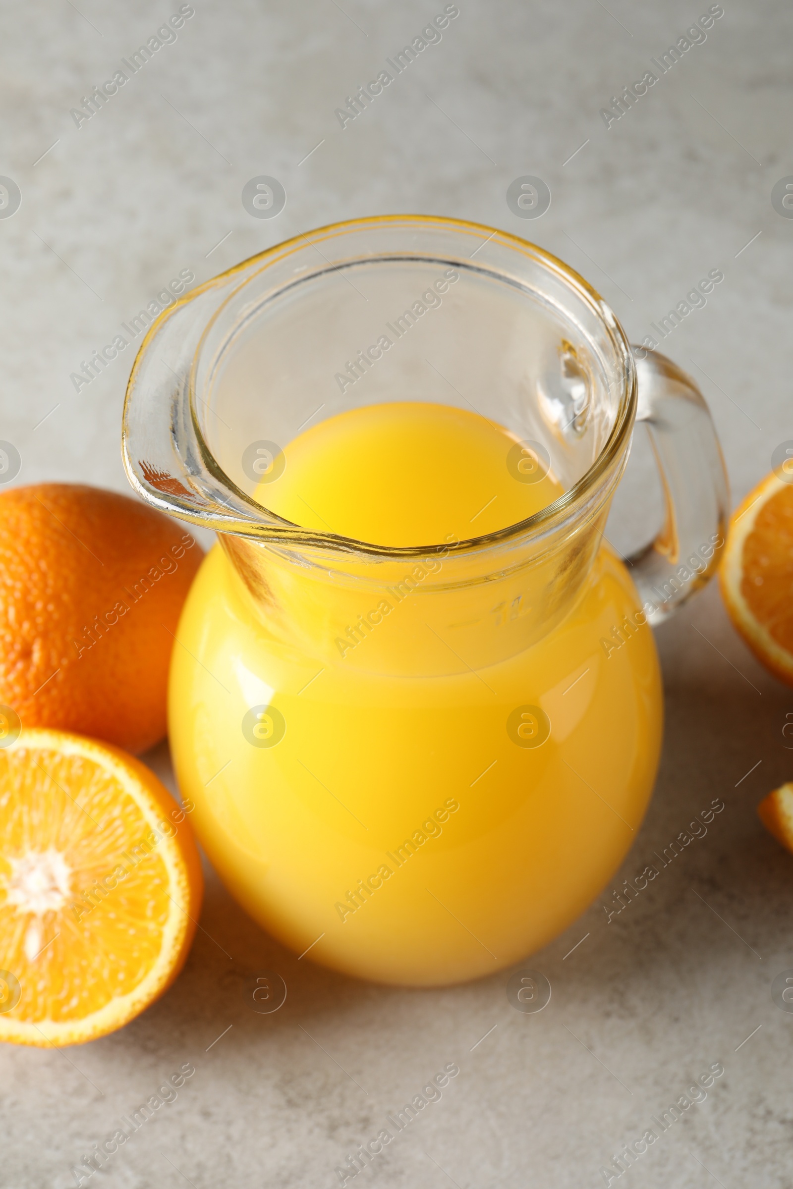 Photo of Tasty orange juice in jug and citrus fruits on light textured table