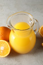 Tasty orange juice in jug and citrus fruits on light textured table