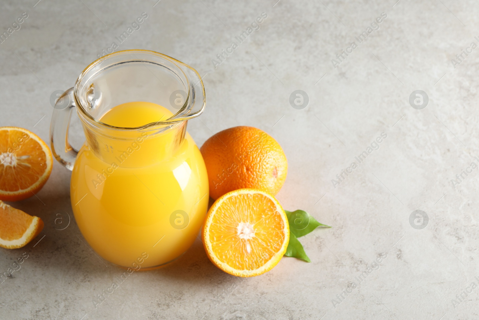 Photo of Tasty orange juice in jug and citrus fruits on light textured table. Space for text