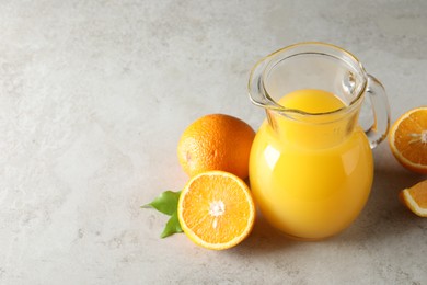 Tasty orange juice in jug and citrus fruits on light textured table. Space for text