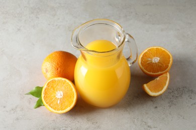 Photo of Tasty orange juice in jug and citrus fruits on light textured table