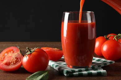 Photo of Pouring tasty tomato juice into glass at wooden table with vegetables, closeup