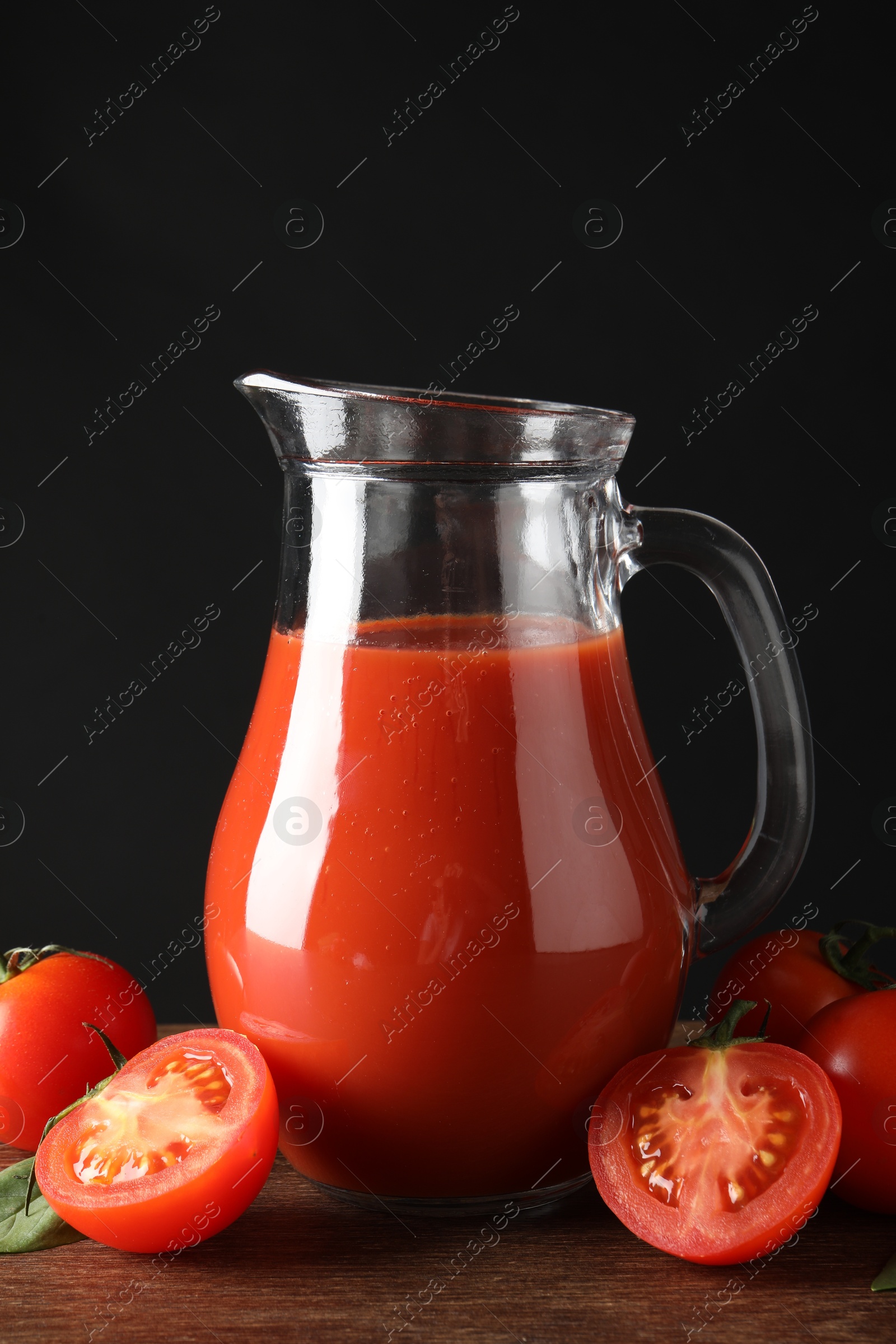 Photo of Tasty tomato juice in jug and vegetables on wooden table against black background