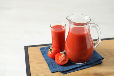 Tasty tomato juice in jug, glass and vegetable on wooden table against white background. Space for text