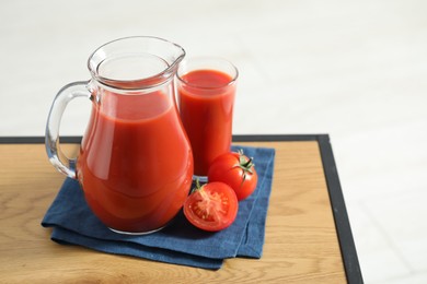 Tasty tomato juice in jug, glass and vegetable on wooden table against white background. Space for text