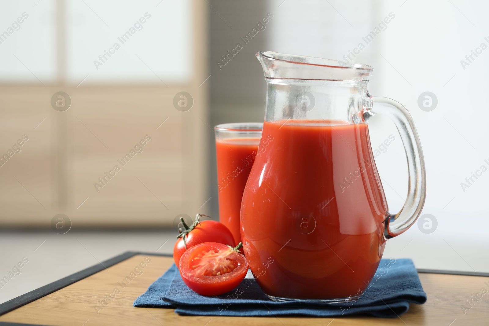 Photo of Tasty tomato juice in jug, glass and vegetable on wooden table indoors. Space for text