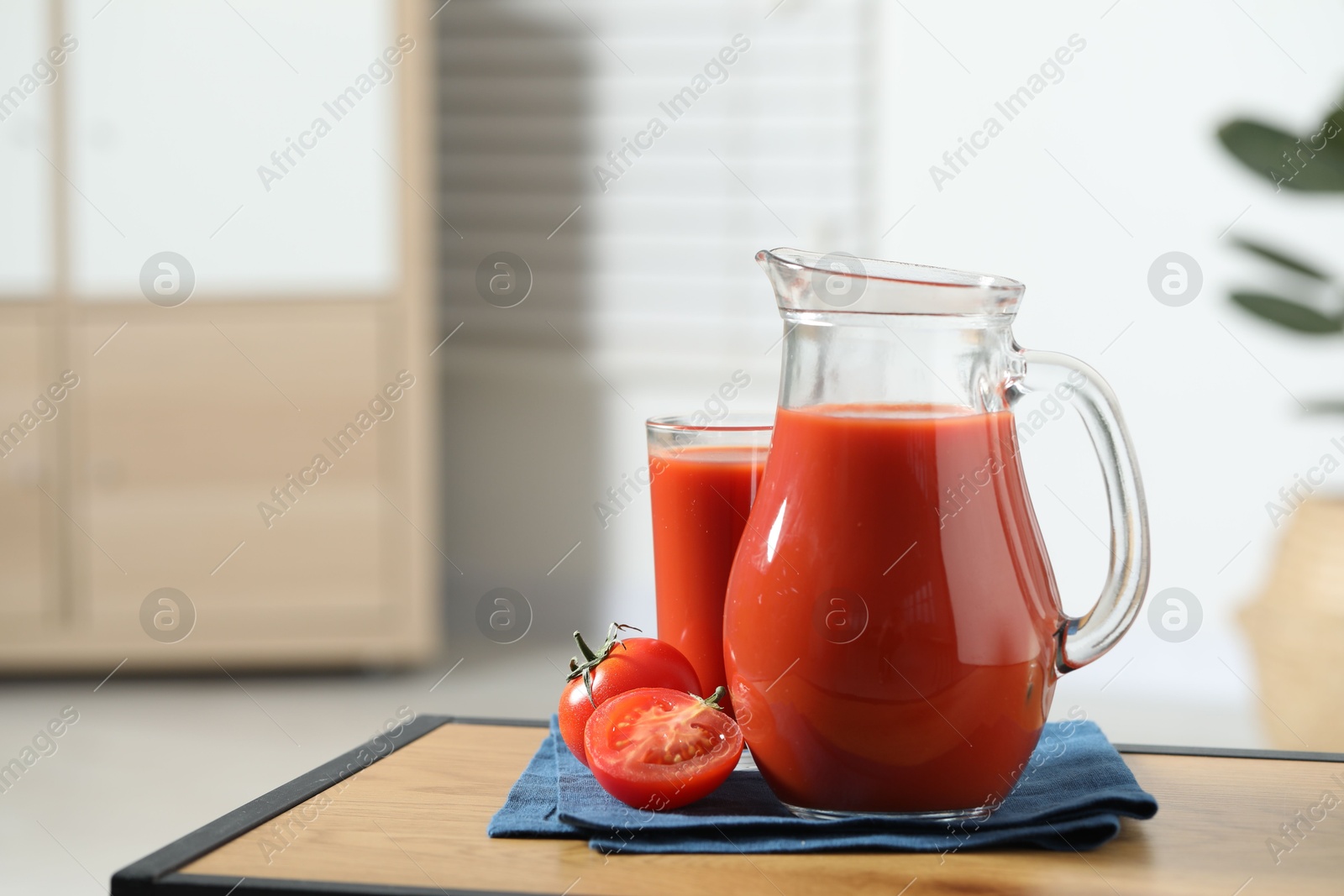 Photo of Tasty tomato juice in jug, glass and vegetable on wooden table indoors. Space for text