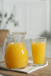 Tasty orange juice in jug and glass on wooden table