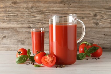 Photo of Tasty tomato juice in jug, basil leaves, peppercorns and vegetables on light wooden table indoors