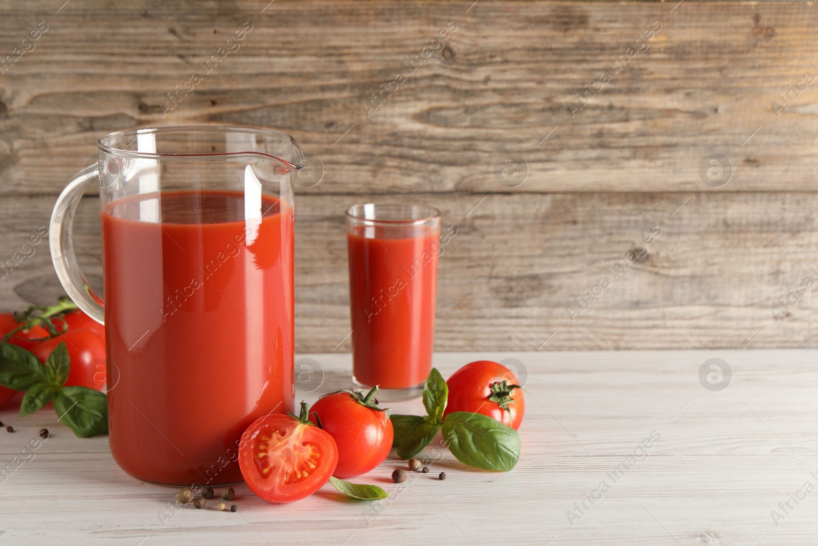 Photo of Tasty tomato juice in jug, basil, peppercorns and vegetables on light wooden table indoors. Space for text