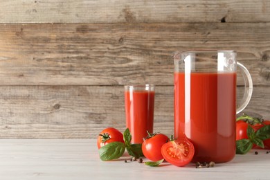 Photo of Tasty tomato juice in jug, basil, peppercorns and vegetables on light wooden table indoors. Space for text