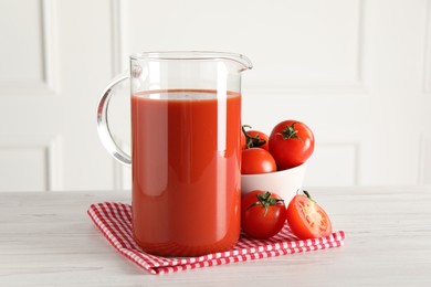 Photo of Tasty tomato juice in jug and vegetables on light wooden table indoors