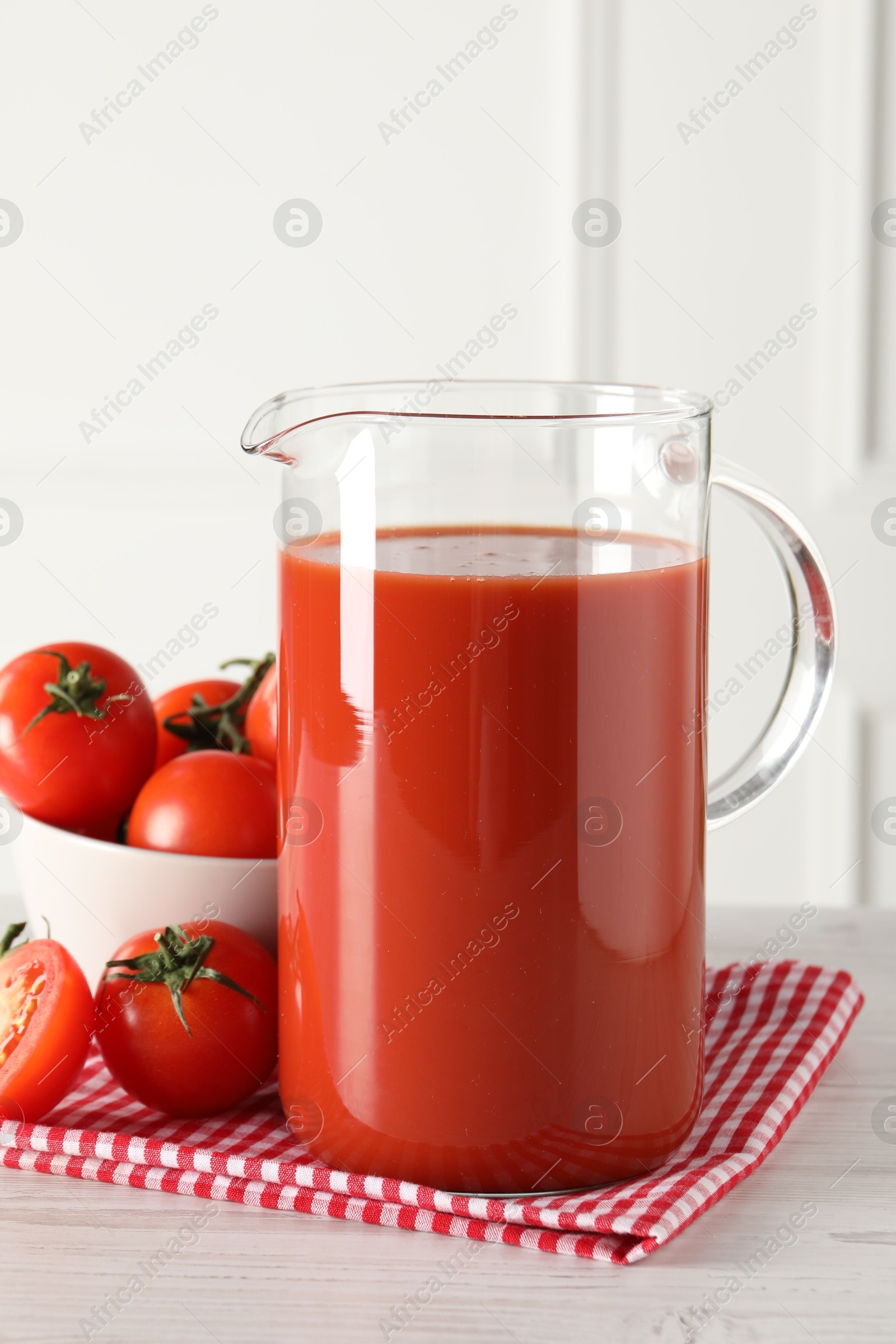 Photo of Tasty tomato juice in jug and vegetables on light wooden table indoors