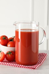 Photo of Tasty tomato juice in jug and vegetables on light wooden table indoors