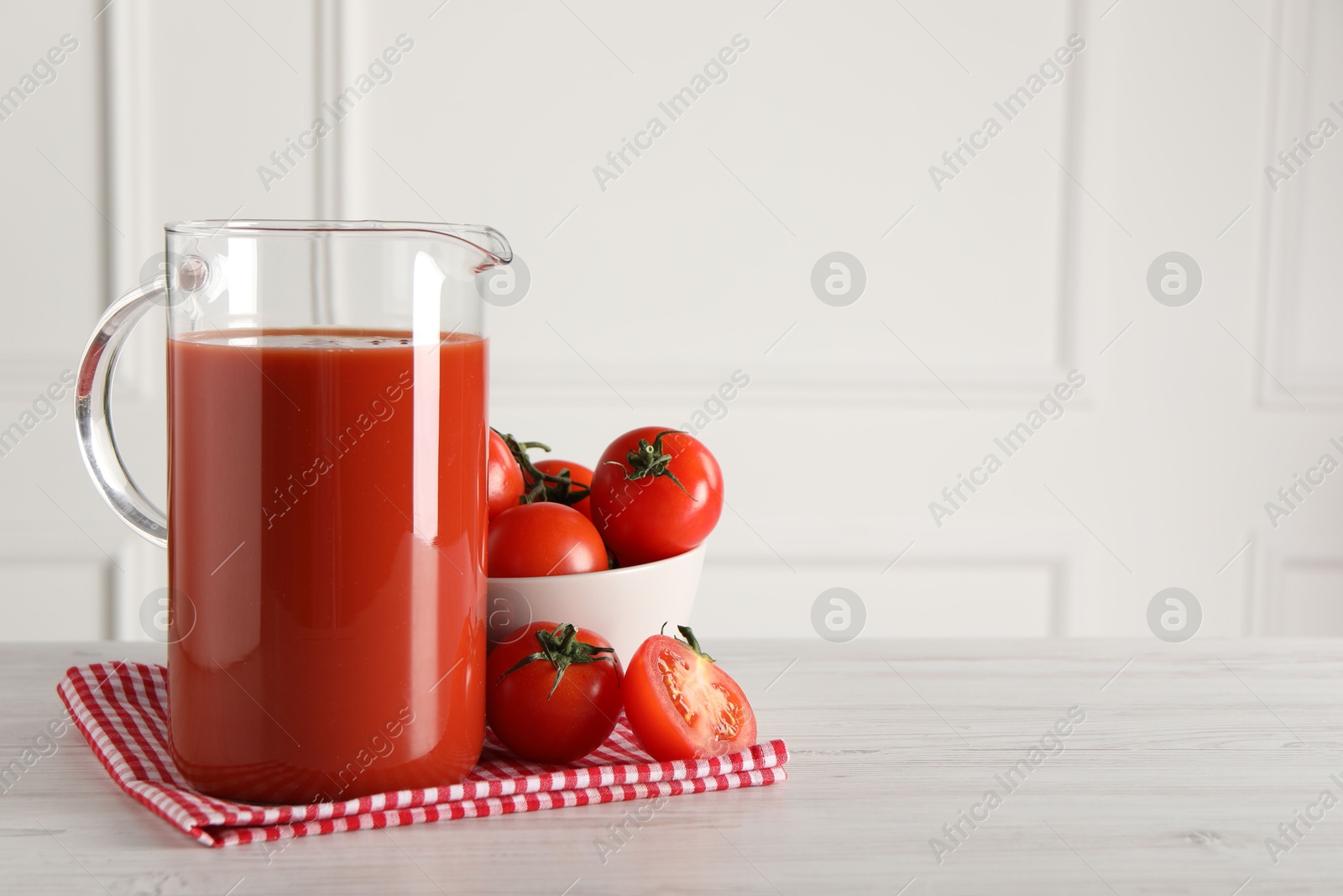 Photo of Tasty tomato juice in jug and vegetables on light wooden table indoors. Space for text