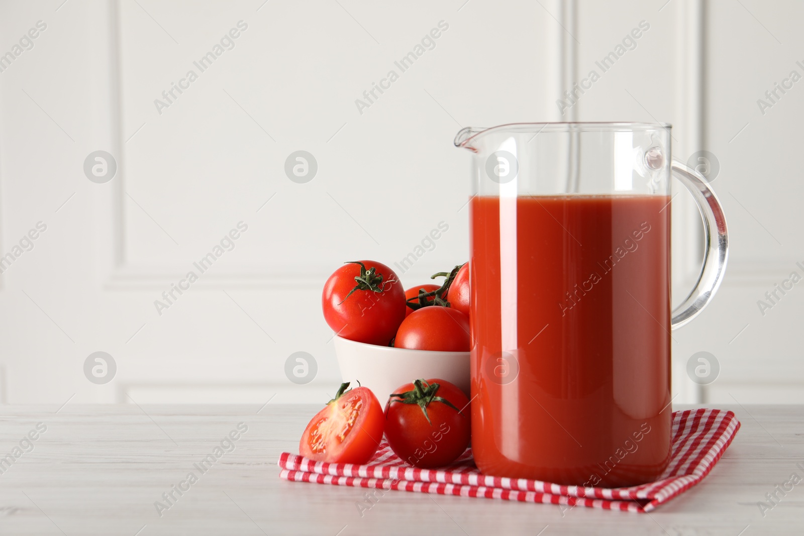 Photo of Tasty tomato juice in jug and vegetables on light wooden table indoors. Space for text