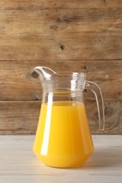 Photo of Tasty orange juice in jug on light wooden table