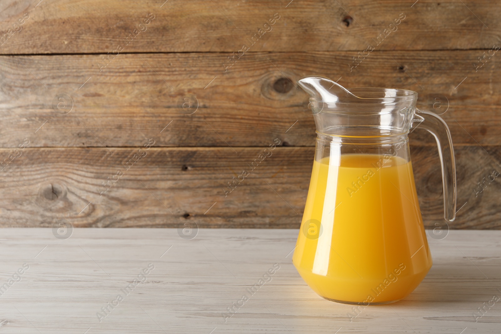 Photo of Tasty orange juice in jug on light wooden table. Space for text