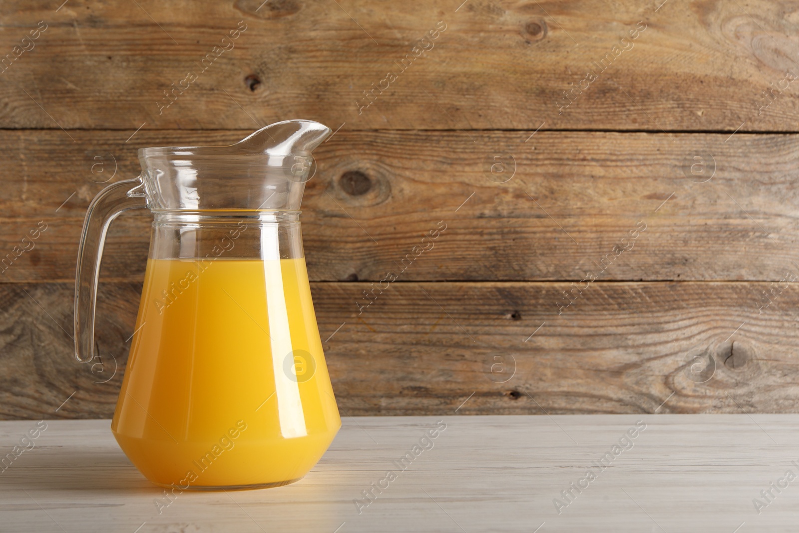 Photo of Tasty orange juice in jug on light wooden table. Space for text