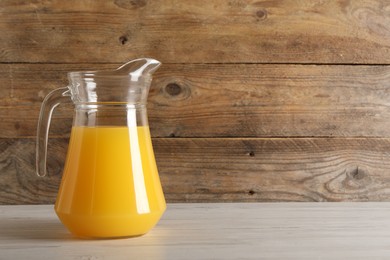 Tasty orange juice in jug on light wooden table. Space for text