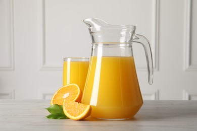 Tasty orange juice in jug, glass and citrus fruit on light wooden table