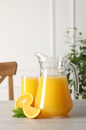 Photo of Tasty orange juice in jug, glass and citrus fruit on light wooden table