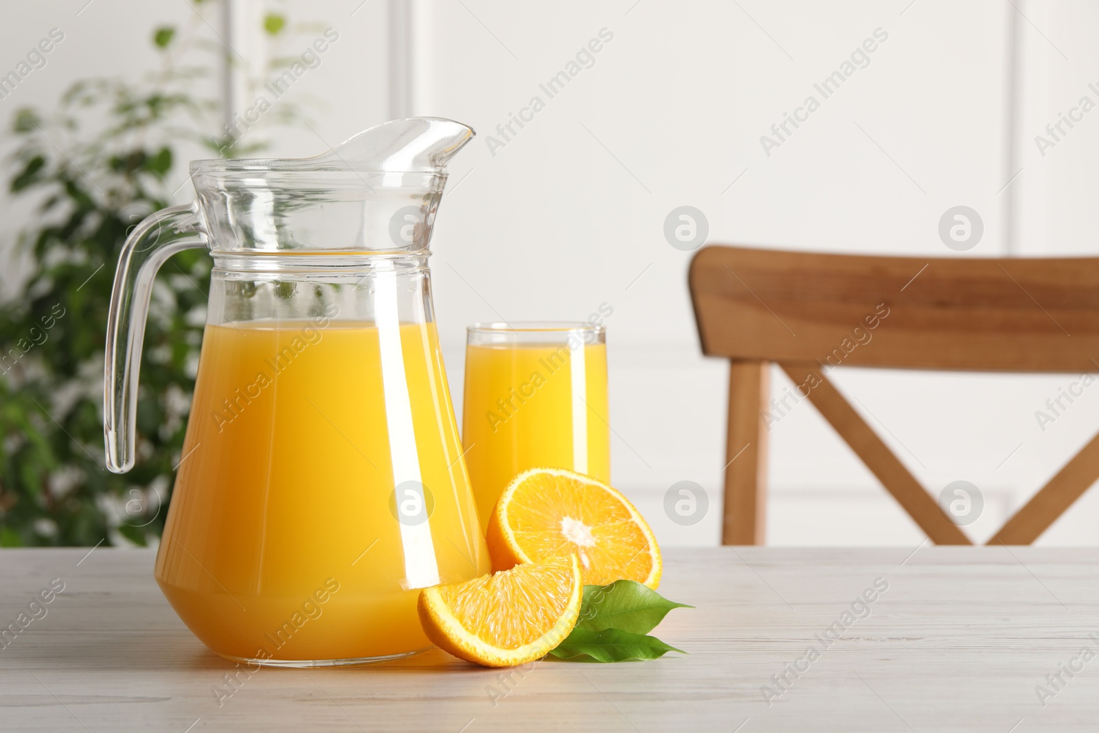 Photo of Tasty orange juice in jug, glass and citrus fruit on light wooden table. Space for text