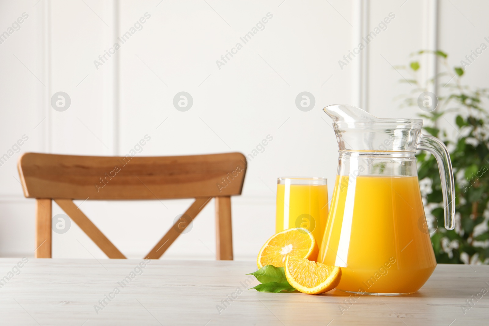 Photo of Tasty orange juice in jug, glass and citrus fruit on light wooden table. Space for text