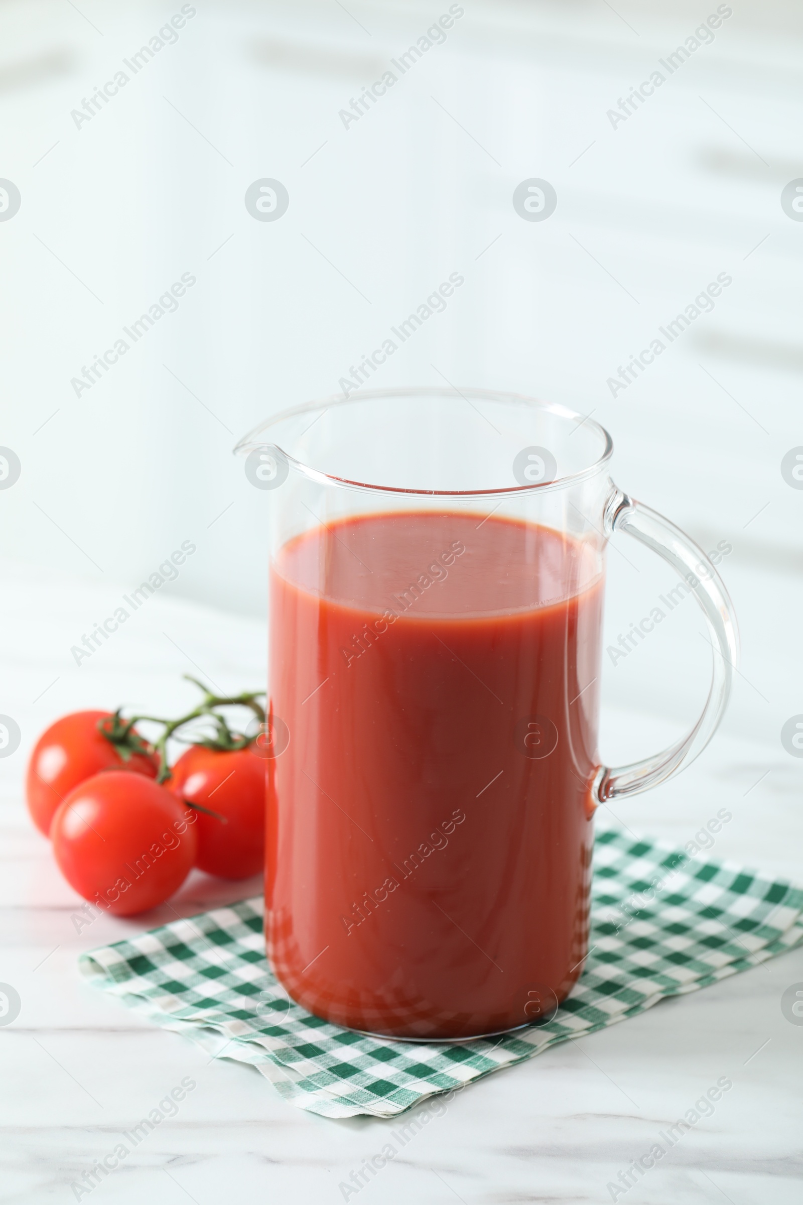 Photo of Tasty tomato juice in jug and vegetables on white marble table