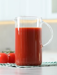 Tasty tomato juice in jug and vegetables on white table