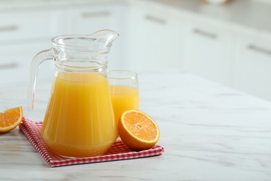 Photo of Tasty orange juice in jug, glass and citrus fruit on white marble table. Space for text