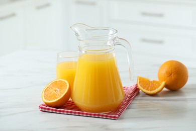 Tasty orange juice in jug, glass and citrus fruits on white marble table