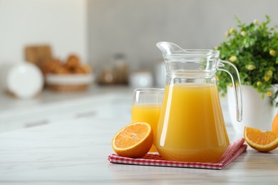 Tasty orange juice in jug, glass and citrus fruit on white marble table. Space for text