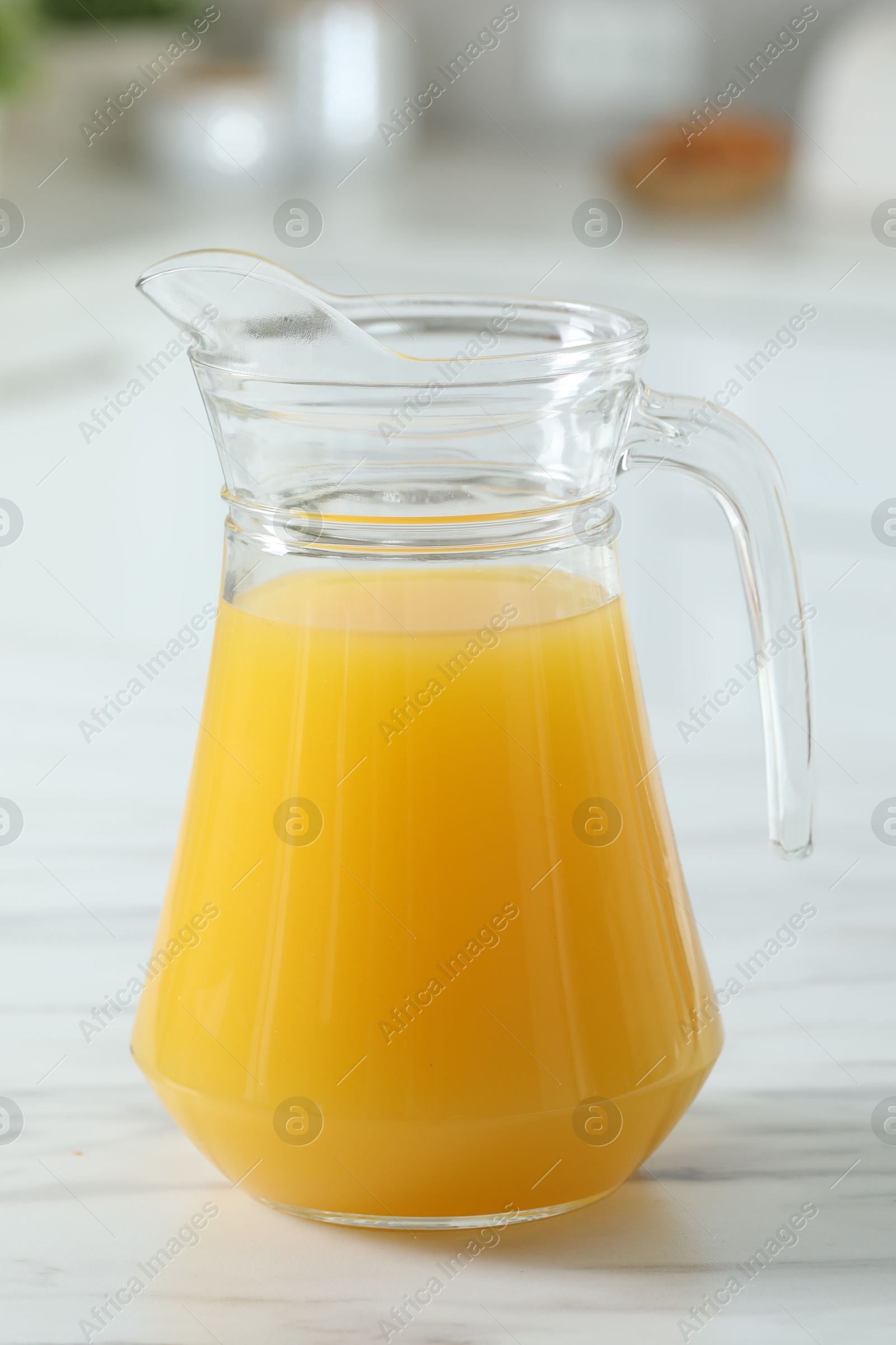 Photo of Tasty orange juice in jug on white marble table, closeup