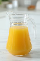 Photo of Tasty orange juice in jug on white marble table, closeup