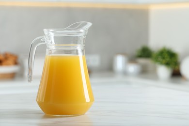 Photo of Tasty orange juice in jug on white marble table. Space for text