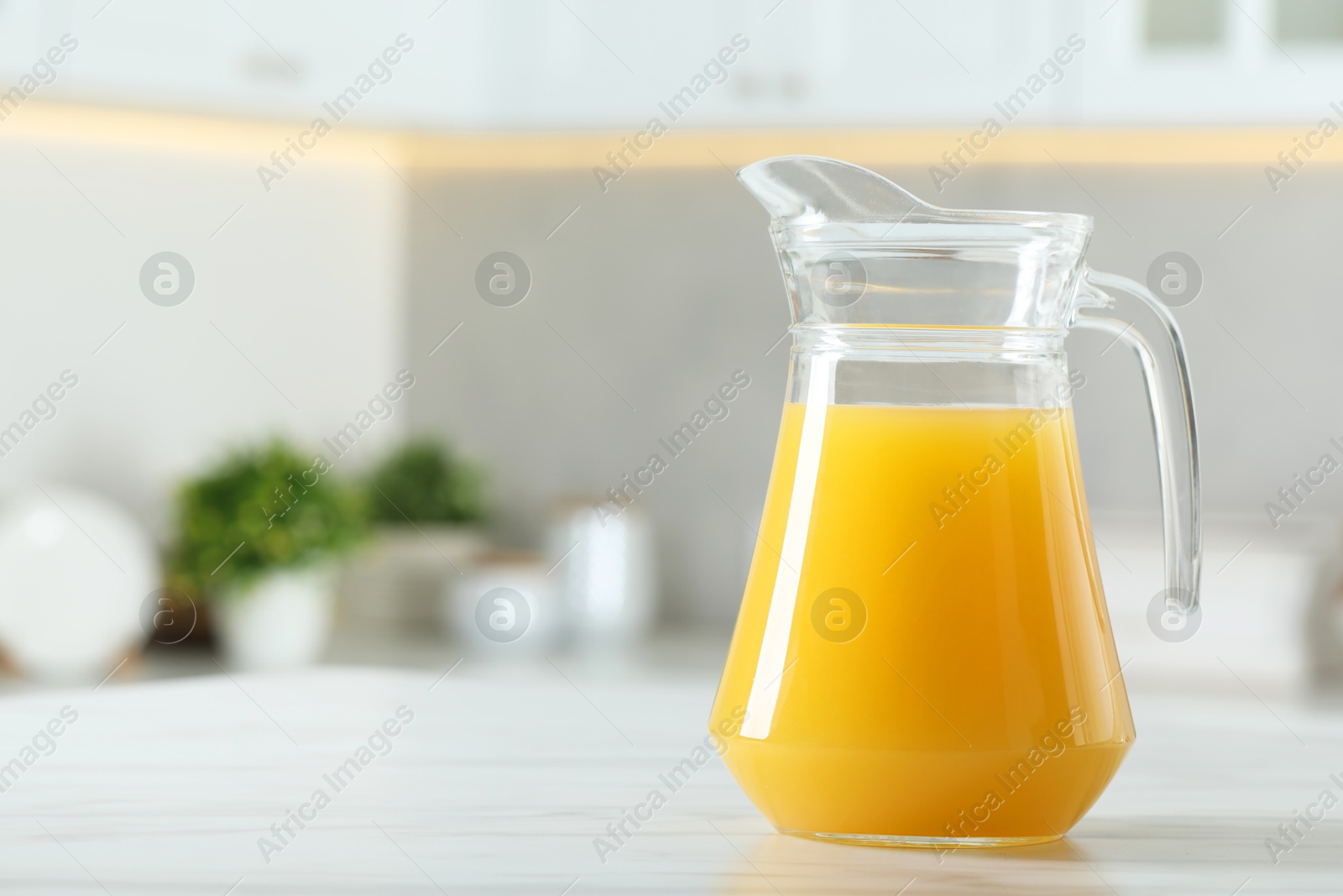 Photo of Tasty orange juice in jug on white marble table. Space for text