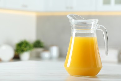 Photo of Tasty orange juice in jug on white marble table. Space for text