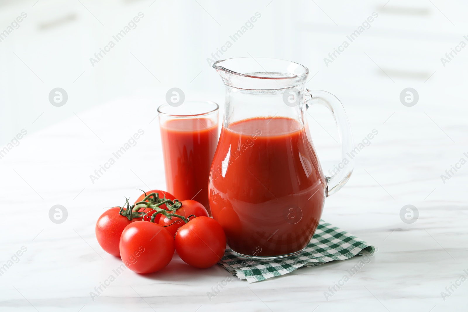 Photo of Tasty tomato juice in jug, glass and vegetables on white marble table