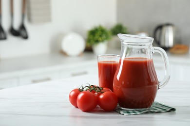 Tasty tomato juice in jug, glass and vegetables on white marble table. Space for text