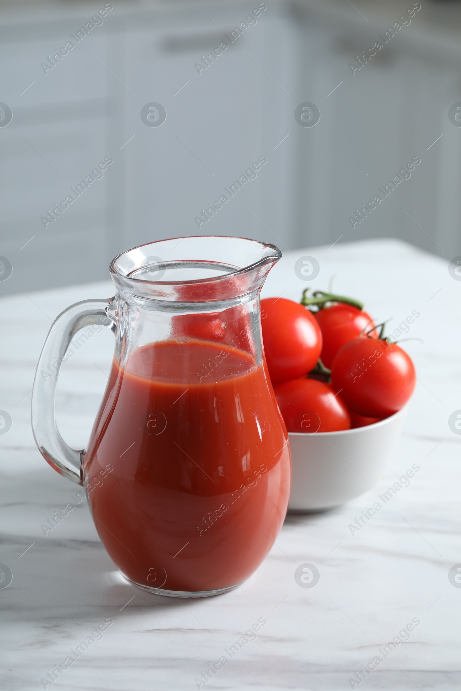 Photo of Tasty tomato juice in jug and vegetables on white marble table