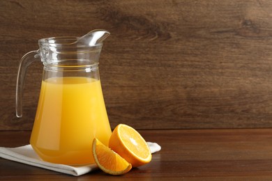 Photo of Tasty orange juice in jug and citrus fruit on wooden table. Space for text