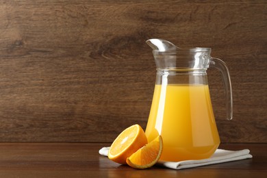 Photo of Tasty orange juice in jug and citrus fruit on wooden table. Space for text