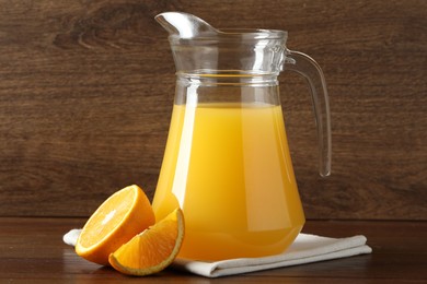 Photo of Tasty orange juice in jug and citrus fruit on wooden table, closeup