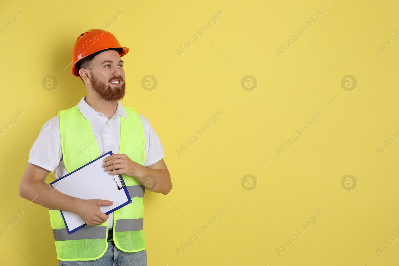 Photo of Engineer in hard hat with clipboard on yellow background, space for text