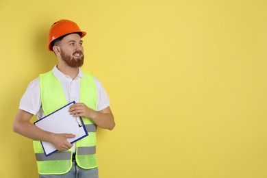 Photo of Engineer in hard hat with clipboard on yellow background, space for text