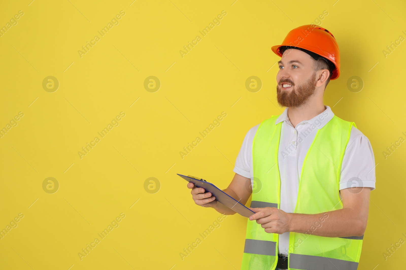 Photo of Engineer in hard hat with clipboard on yellow background, space for text